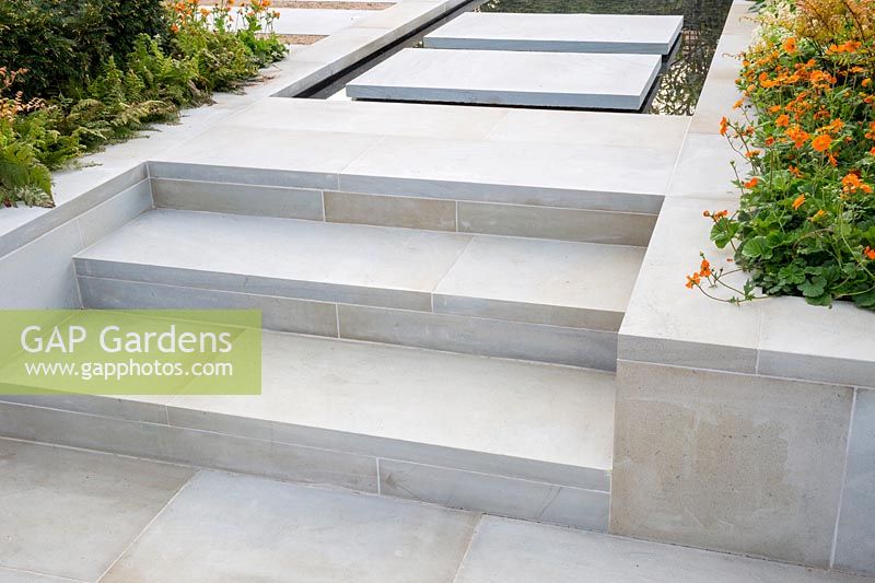 Large sawn Yorkstone steps leading up to floating stepping stone slabs over a water feature pool. The Sunken Retreat. RHS Malvern Spring Festival, 2016. Design: Ann Walker for Graduate Gardeners
