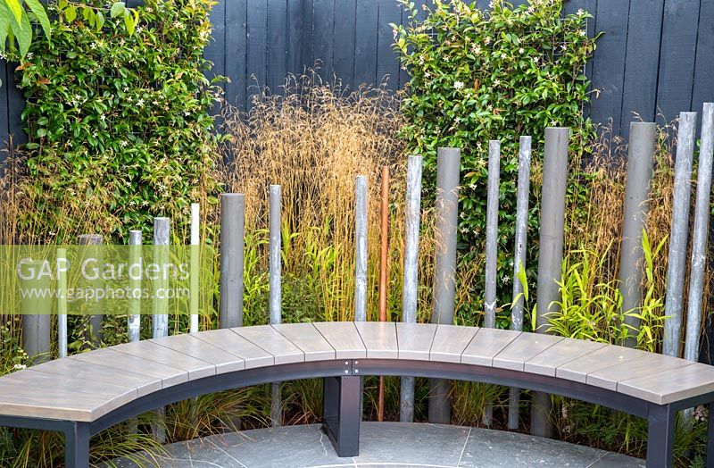 A modern garden bench on stone paved patio. The Macmillan Legacy Garden, RHS Tatton Park Flower Show, 2017. Designer: Lara Behr 