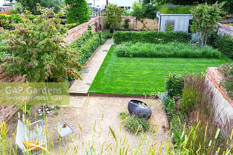 An overview of a contemporary city garden with gravelled seating area, raised lawn and wildflower border