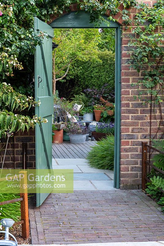 The entrance to a contemporary walled cottage garden with deck, seating and containers.