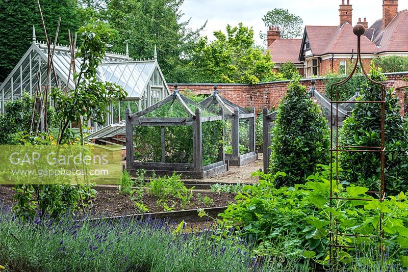 A formal kitchen garden with bespoke oak cloches to protect vulnerable crops, bay tree cones to add permanence, and an Alitex greenhouse for growing tomatoes, chilli peppers and annuals.