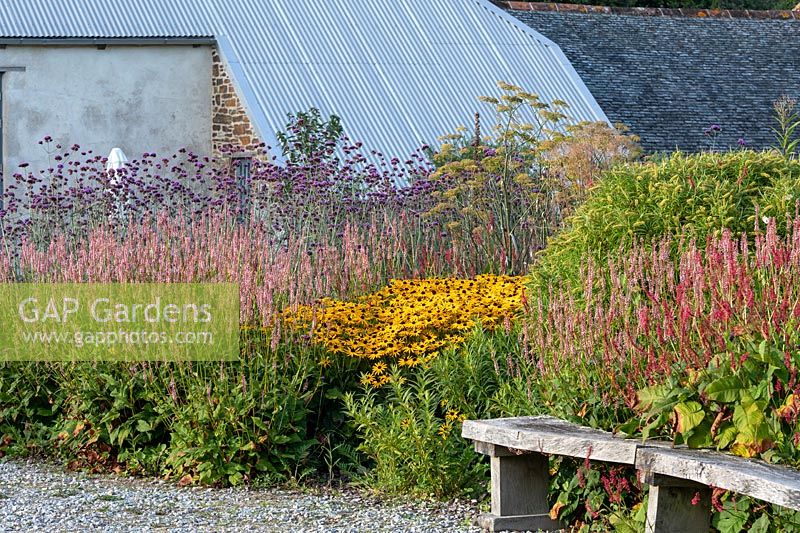 Perennial flower bed with rustic oak bench and converted old farm buildings behind