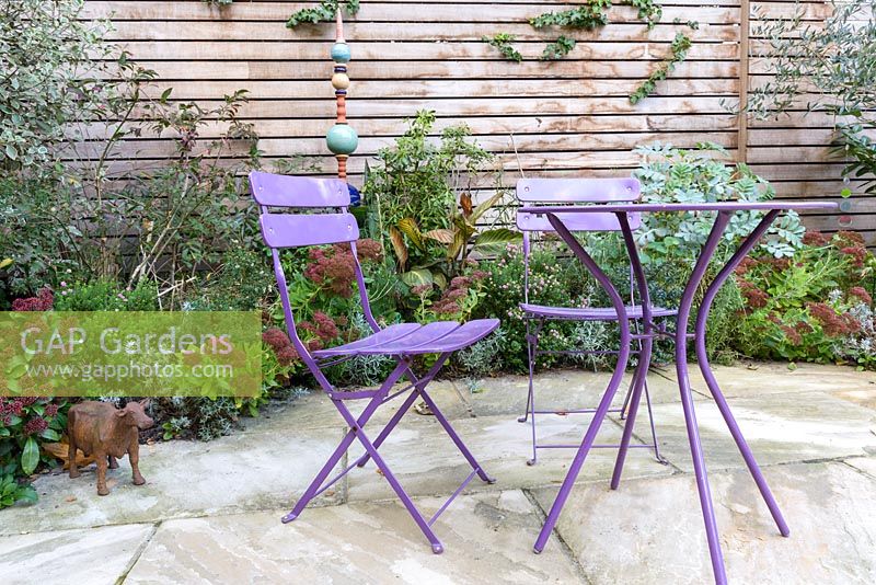Low maintenance  city garden - paved patio with violet metal bistro chairs and table and slated cedar fencing