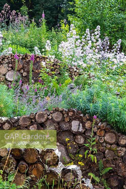 Insect and wildlife friendly log walls within naturalistic borders planted with perennials.