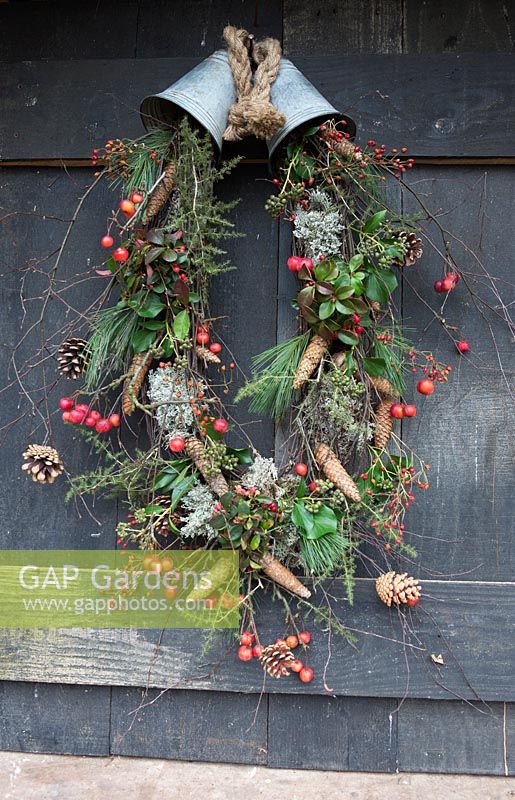 Rustic Christmas wreath made with a mix of rosehips, crab apples, pinecones and foliage hanging from two metal bells. Styling by Marieke Nolsen