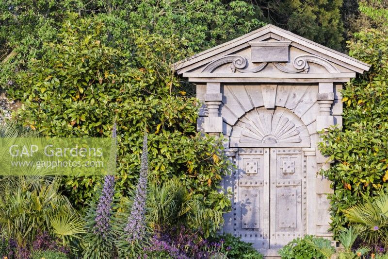The Italian Gate carved from green oak and based on designs by Inigo Jones for Arundel House in London from the early 17th century in the Collector Earl's Garden at Arundel Castle, West Sussex in May. Framed by echiums and palms.