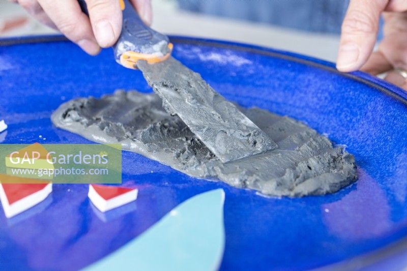 Close up of woman using a scraper to spread grout around a plate