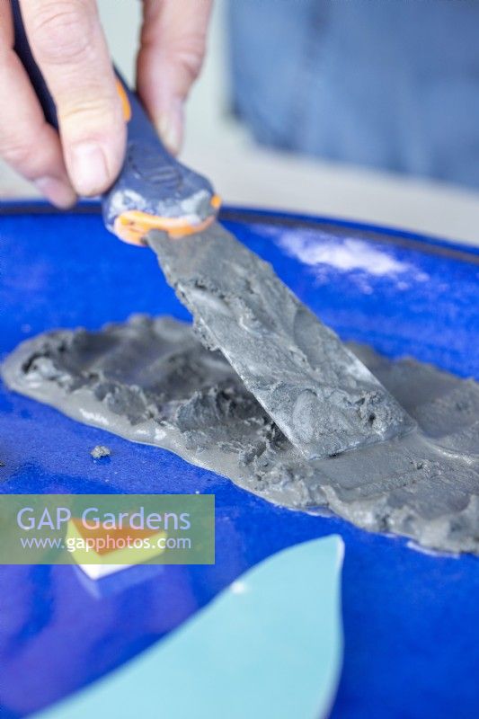 Close up of woman using a scraper to spread grout around a plate