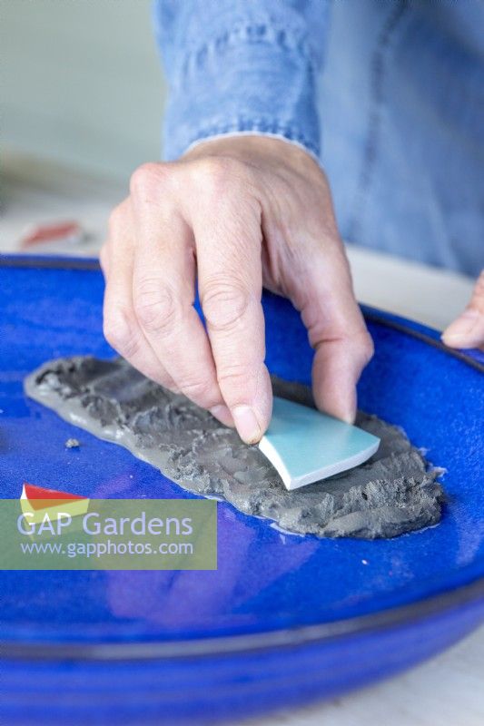 Close up of woman placing pieces of smashed plate on the grout