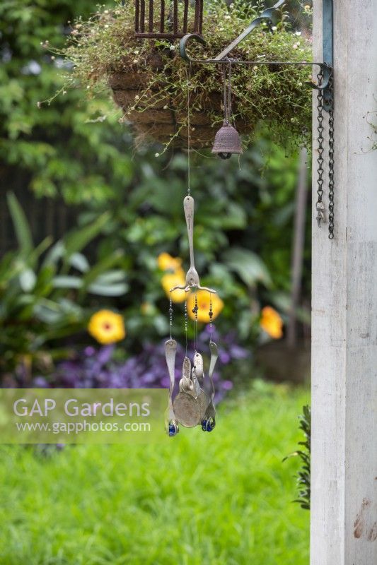 A handmade windchime made from repurposed forks and spoons and blue glass marbles suspended from a hanging basket in a backyard.