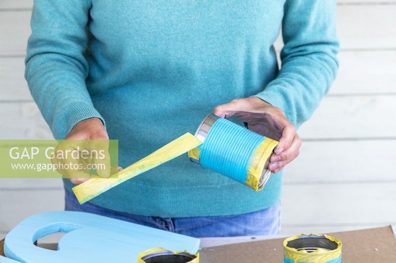 Woman taking the masking tape off of the painted tin cans