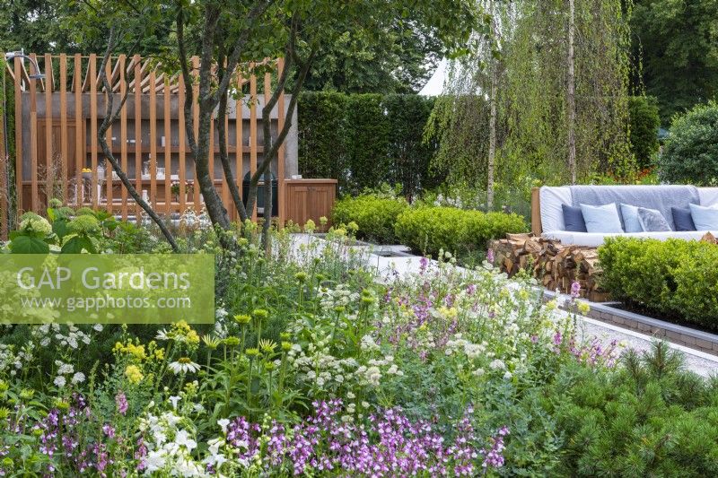 The Viking Friluftsliv Garden. A multi-stemmed amelanchier shades a bed of astrantias, penstemon, coneflowers, salvias, gaura and thalictrum. On the other side of the box-edged rill is a seating area, shaded by tall birch trees.