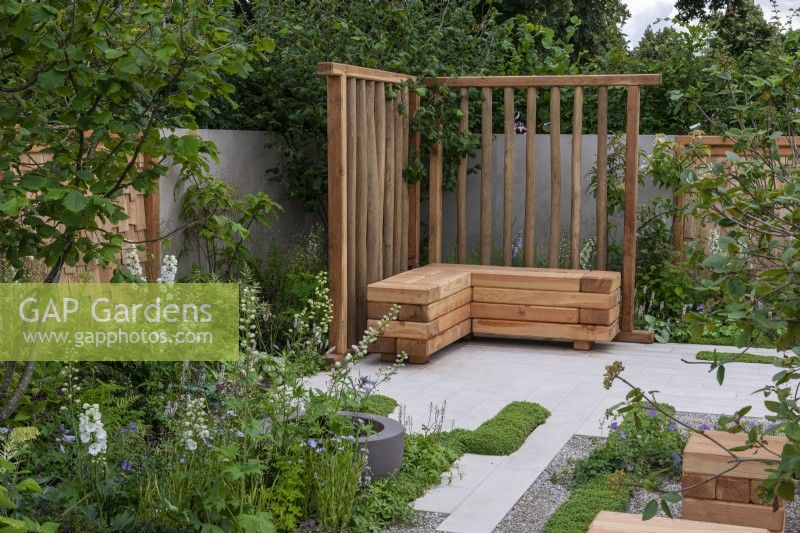 The Communication Garden. A tranquil refuge with woodland planting and native wayfaring and hazel trees. The flooring is laid in planking and gravel. Wooden screens and cubes are made from sweet chestnut.