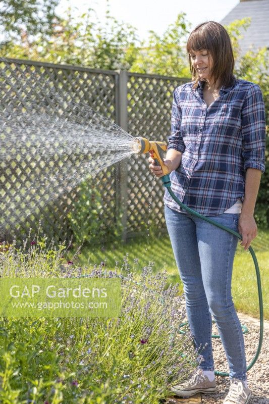 Woman using a hose with a spray gun to water plants