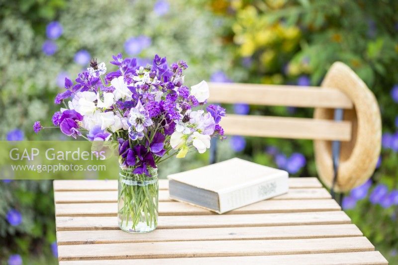 An arrangement of Nigella papillosa 'Delft Blue', Salvia viridis 'Blue Monday', Verbena rigida 'Santos', Lathyrus 'High Scent', 'Pluto' - Sweet Peas in a glass vase