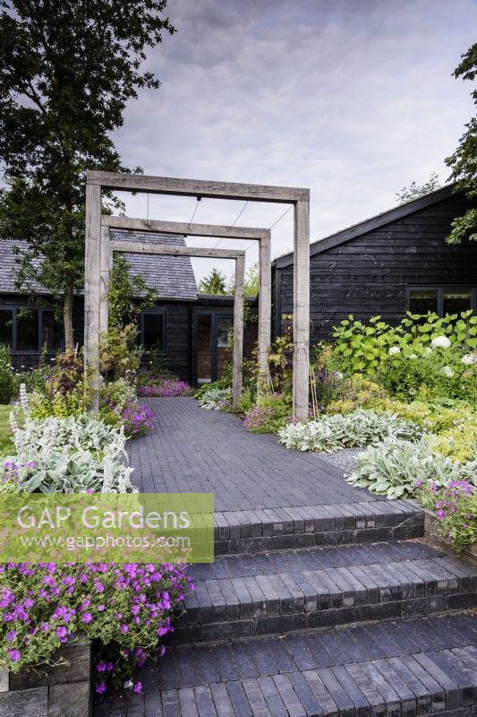 Steps and path of Lucca brick pavers by Chelmer Valley lead towards a simple timber pergola in July