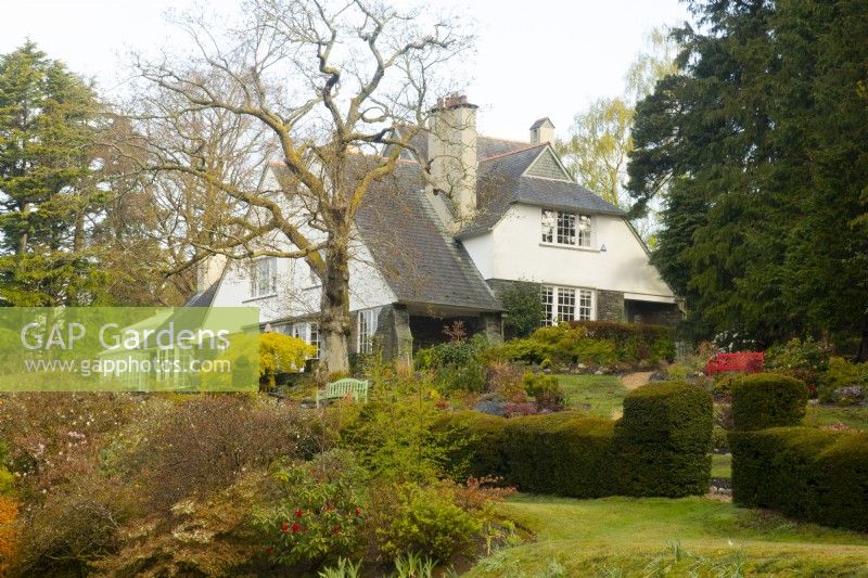 The Arts and Crafts style house on a hill at High Moss surrounded by mixed borders and a topiary hedge - Taxus baccata and a large oak tree - Quercus