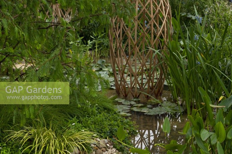 A laminated bamboo grid structure surrounded by a pool filled with aquatic plants in the Guangzhou China: Guangzhou Garden, winner of the Best Show Garden award at the RHS Chelsea Flower Show 2021