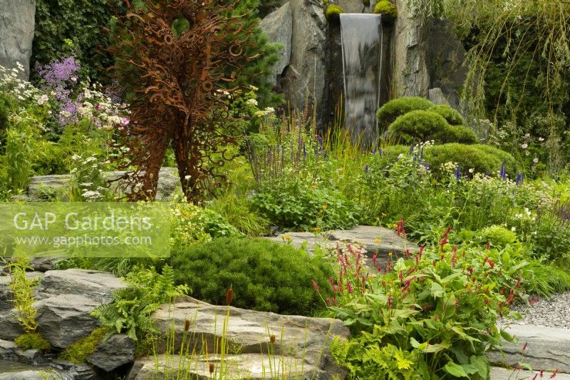 60 Degrees East, a garden between continents, a figurative metal sculpture beside a waterfall on a hillside surrounded by European and Asian planting.  Sculptures by Penny Hardy