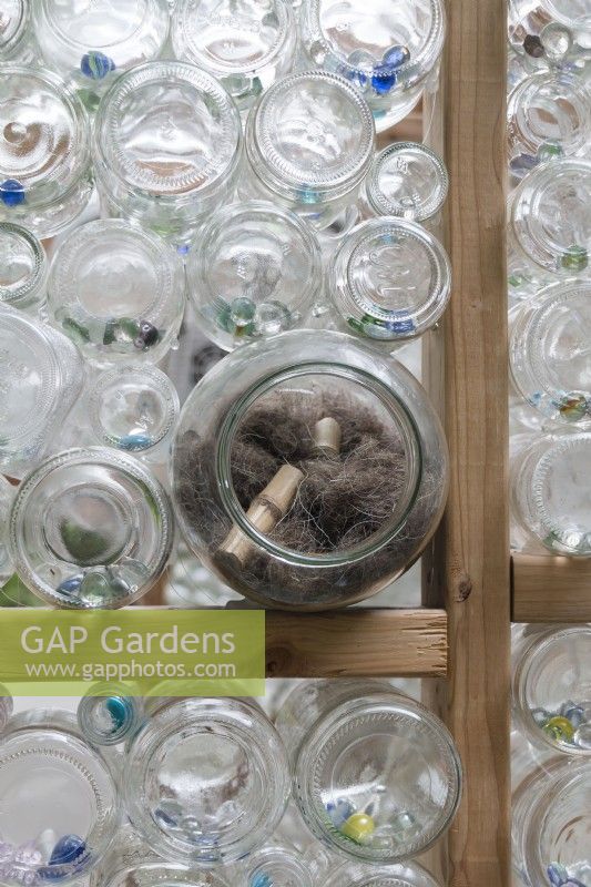 Nesting materials for birds are tucked into outward facing glass jars in recycled greenhouse walls