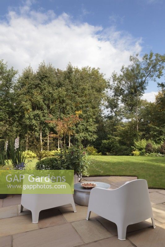 Stone patio area with metal table and modern chairs looking out onto garden - Cheshire - July