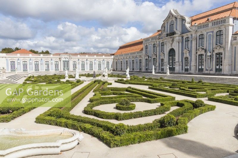 View to palace buildings across the Malta Garden. Low hedges of clipped box with statuary. Queluz, Lisbon, Portugal, September. 