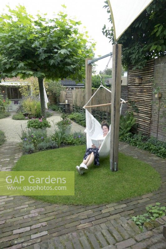 Curvy path of bricks with round shaped lawn and woman sitting and reading in the hammock.