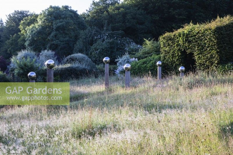 Avenue in meadow of stainless steel globes mounted on wooden pillars. July, Summer. 