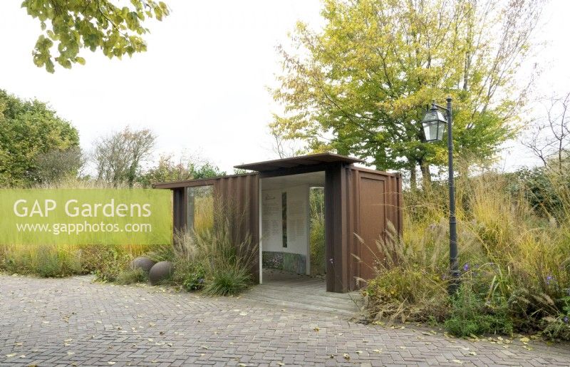 Walk-in Corten steel structure with display boards, set in border of grasses near lamp post.