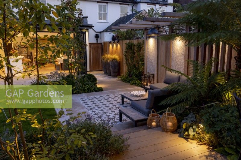 Contemporary garden at night with patio and pergola, looking towards house and kitchen