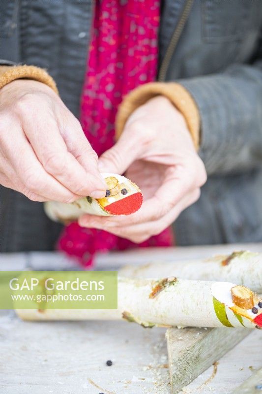 Woman fixing the thin wooden ovals and peppercorns to the sticks with glue as noses and eyes