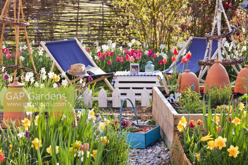 Raised beds and borders with flowering tulips and daffodils, plus vegetables beds. Nearby seating area with deckchairs.