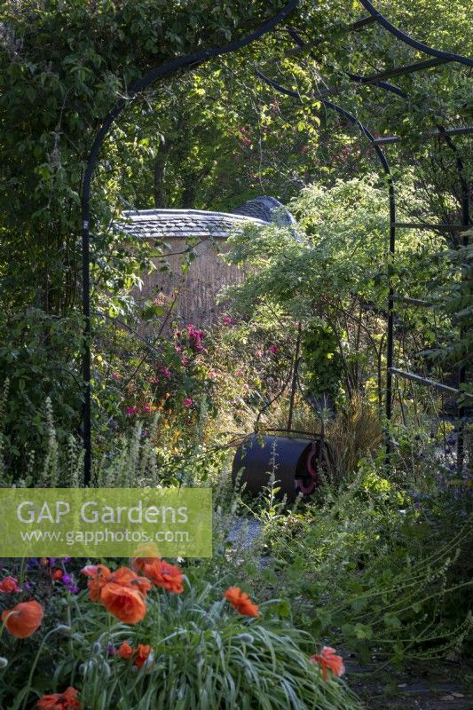 Garden lawn roller seen through arched metal pergola in romantic summer garden