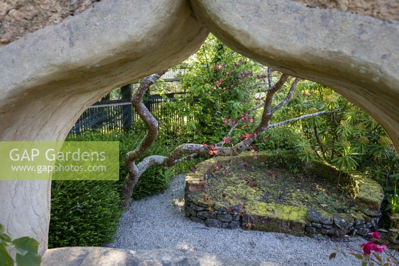 Cob wall structure in garden, with arched window 'peephole' through to secret garden