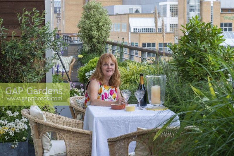 Lynda on her fourth floor balcony surrounded by planters of evergreens and perennials, overlooking the town.