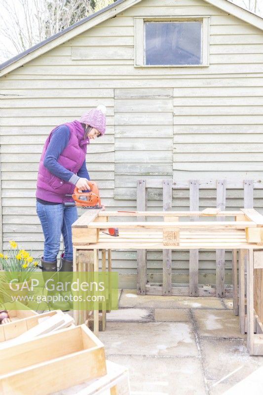 Woman cutting off excess lengths of wood from the pallet