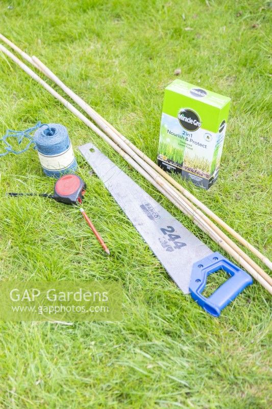 Granular fertiliser, bamboo canes, saw, twine, tape measure and a pencil laid out on the ground