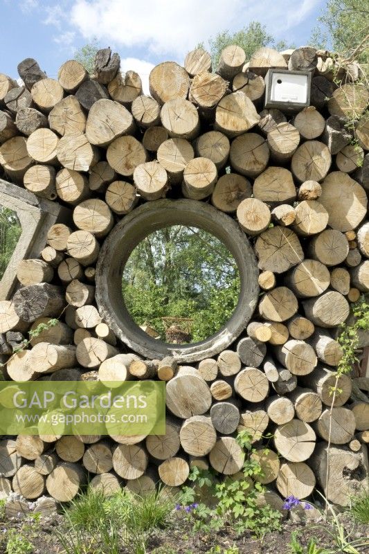 Insects hotels made in wall of stacked tree trunks and concrete drainage pipes. 