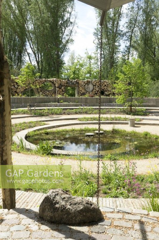 View over The Spiral of Life garden at a garden show with water chain and circular paths over pond with pond planting.