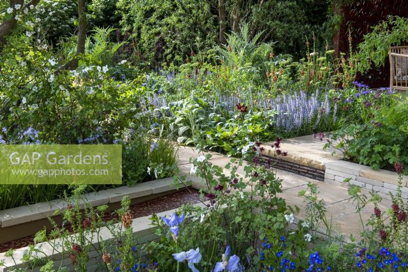 Yorkstone paved path divides colourful borders, step with handmade clay risers and water rill with laser cut insert - Morris  and  Co, RHS Chelsea Flower Show 2022 - Gold Medal