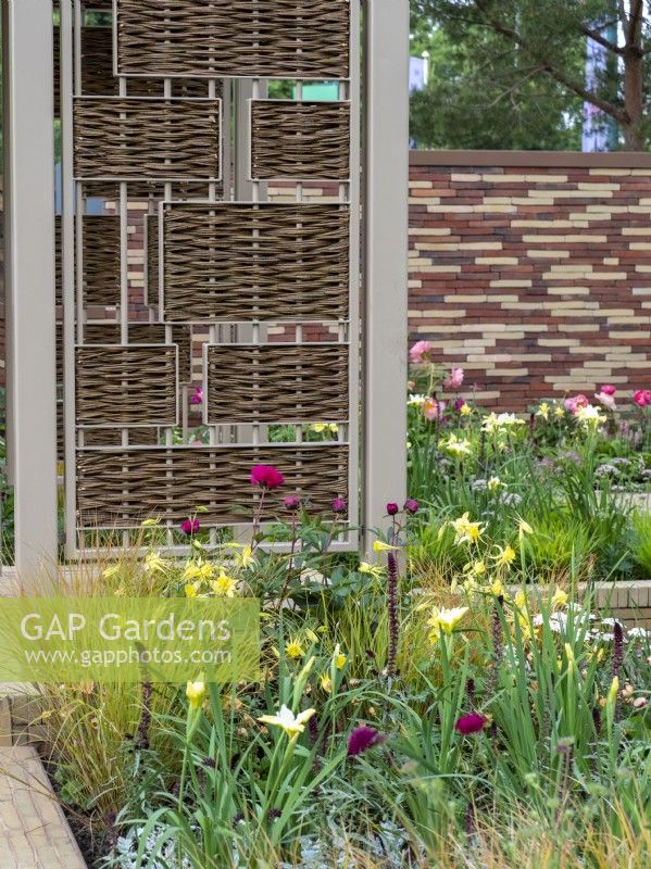 The Stitchers' Garden featuring soft yellows and deep pinks with tapestry walls and willow screens.