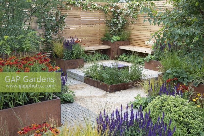 Simple wooden benches overlook a reflective water feature in Lunch Break Garden at RHS Hampton Court Palace Garden Festival 2022