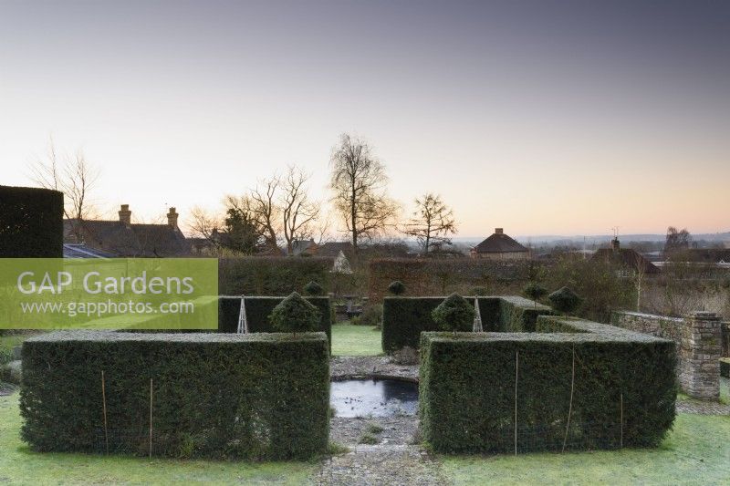 Yew hedges frame a circular pond in a formal town garden in winter