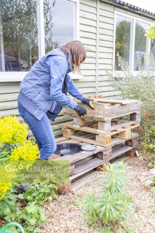 Woman screwing the plank of wood to the side of the pieces of pallet