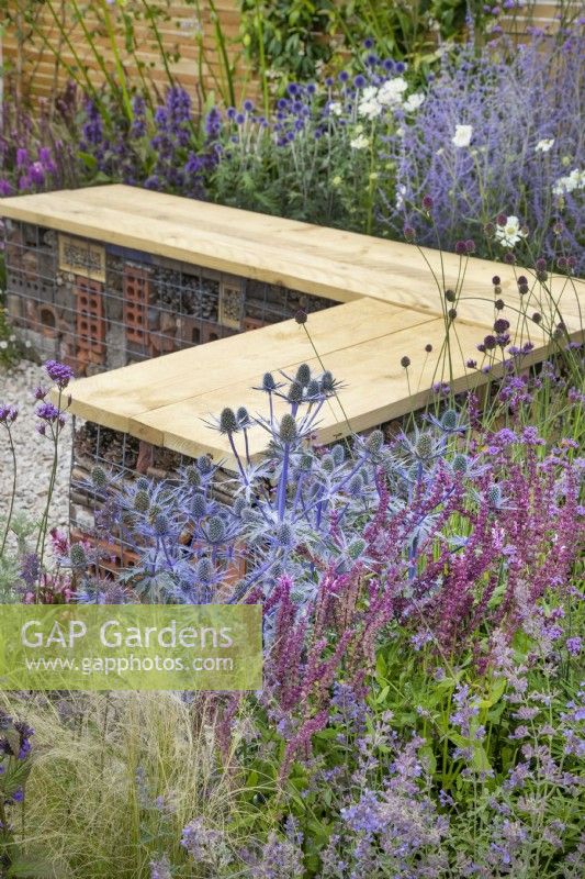 Bench made of gabions with bug hotels and pink and purple themed perennial planting in Turfed Out at RHS Hampton Court Palace Garden Festival 2022