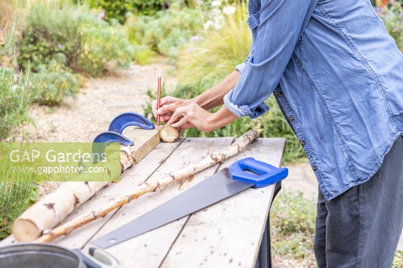 Woman marking a reference point on a block of wood to saw all of the pieces of wood to the same length