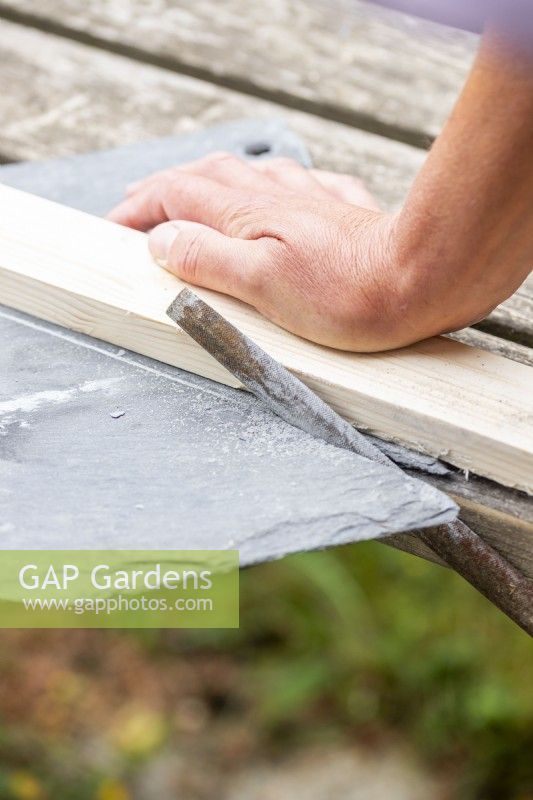 Woman using a length of wood and a file to break the slate along the scored line