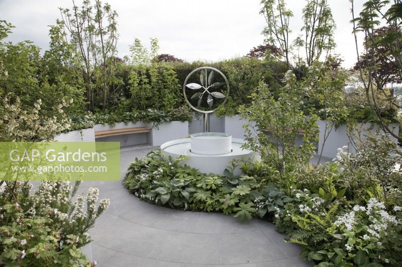 Circular water feature surrounded by green and white planting and circular paving in CRUK Legacy Garden at Malvern Spring Gardening Festival 2022