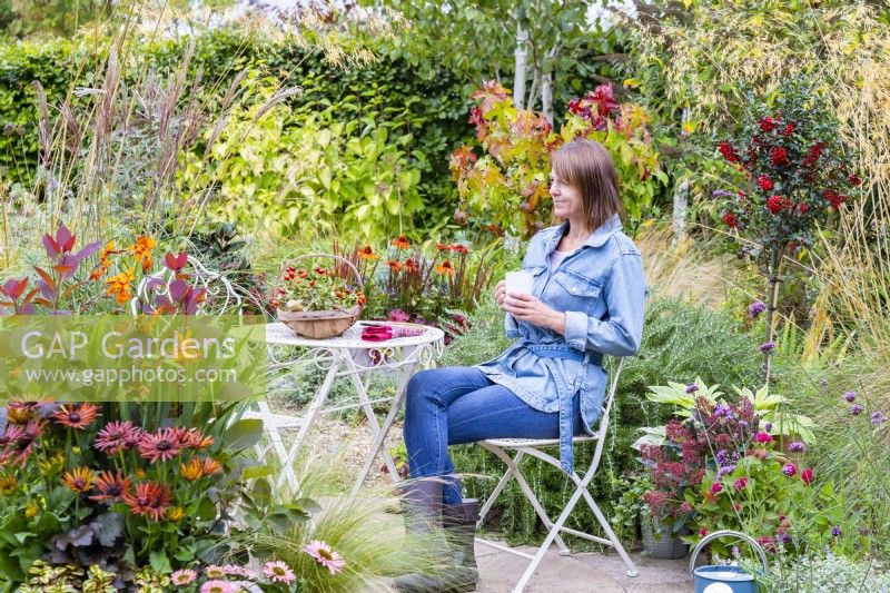 Woman sitting at a table on a patio with a hot drink, surrounded by plants