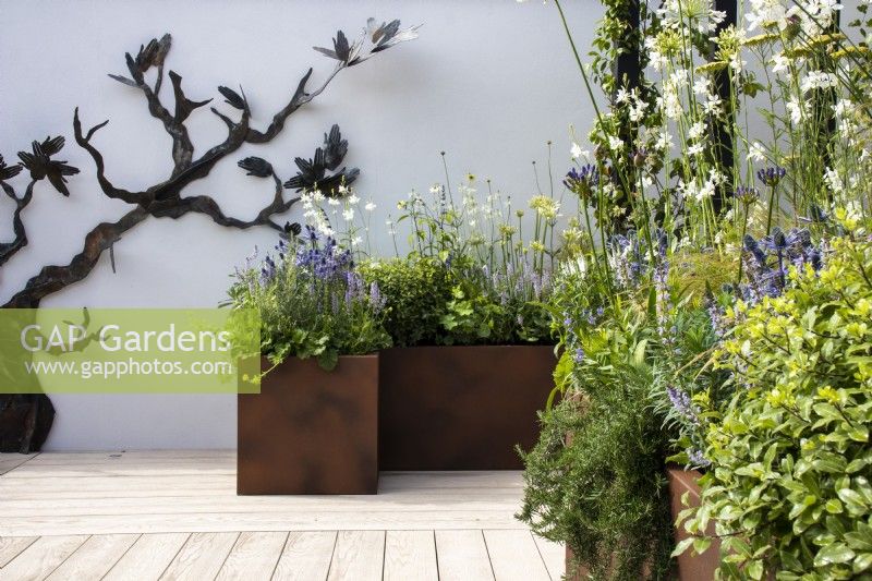 Raised rust-coloured metal planters, with perennials,  'Ovation Hands' sculpture by Emma Rodgers - RHS Hampton Court Palace Garden Festival, London July 2022 - 'John King Brain Tumour Foundation Garden', People's choice show garden - Designer Rhiannon Williams